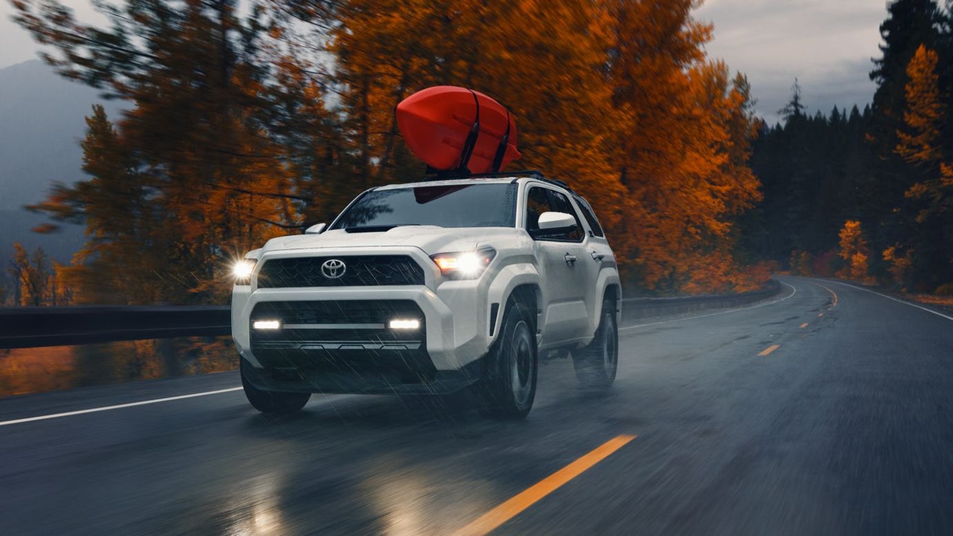 A white Toyota 4Runner driving down the road in autumn, with a red kayak strapped to its roof.