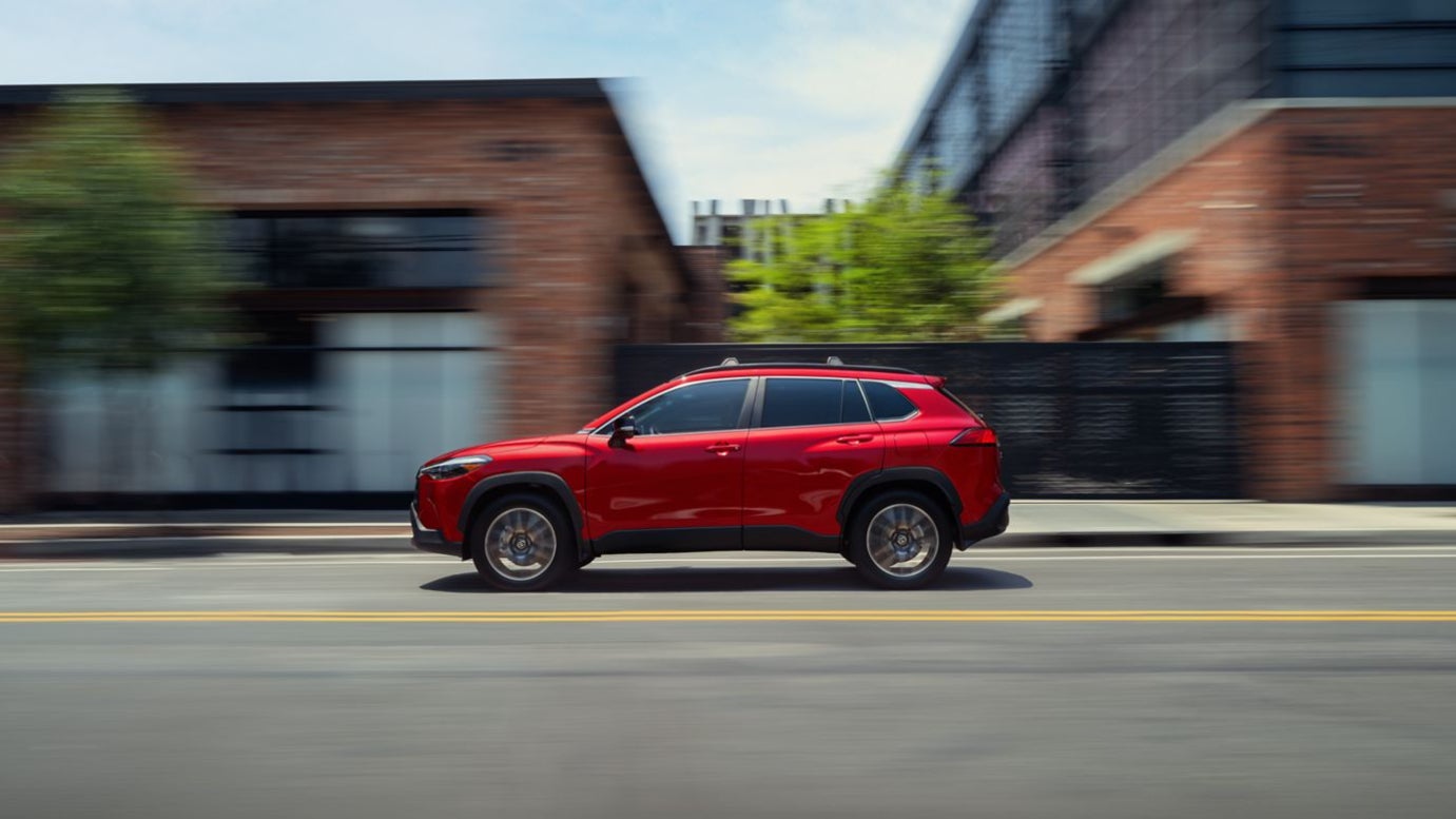 A red Toyota Corolla Cross in profile quickly driving down the street.