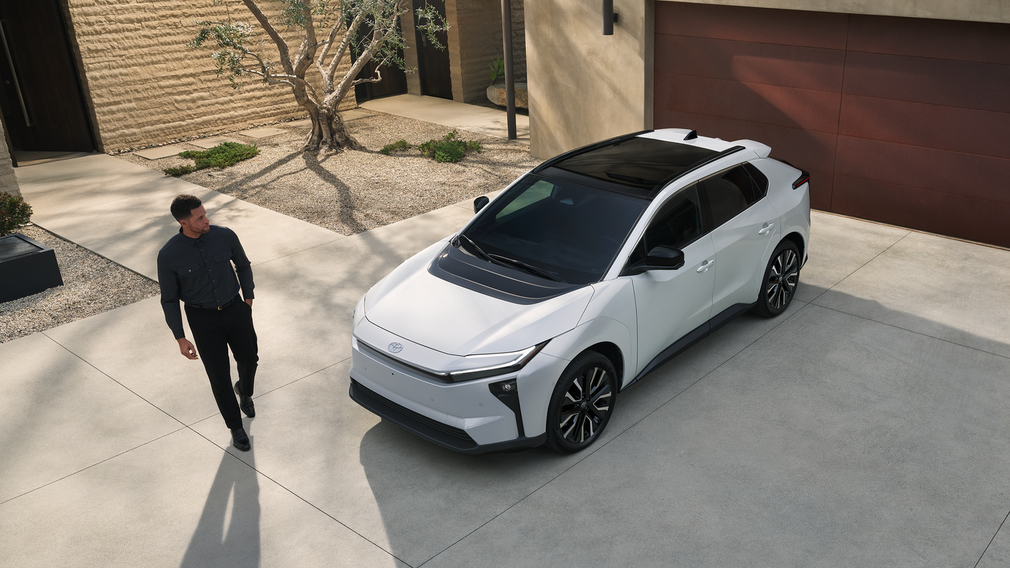 A white Toyota bZ parked in a driveway while a man walks up to it.