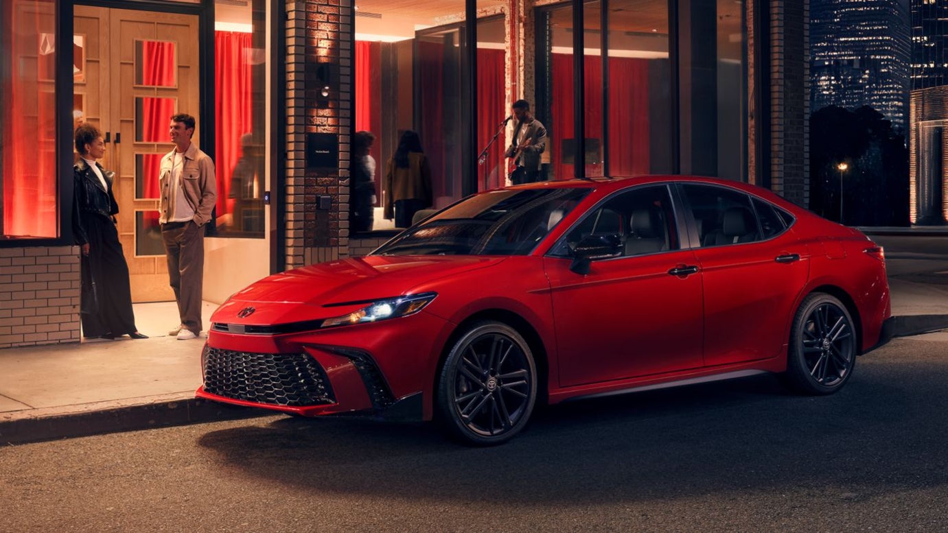 A red Toyota Camry parked by the curb outside a club or restaurant at night.