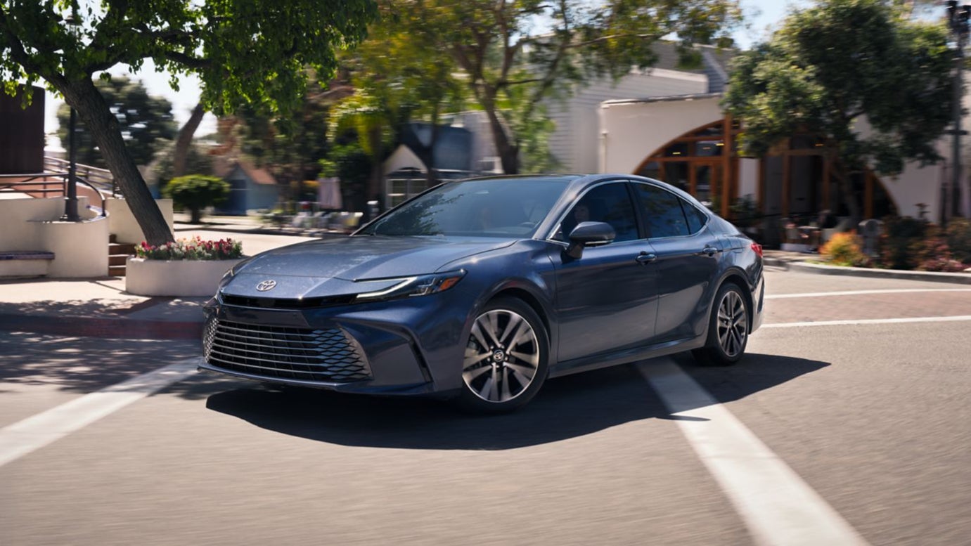 A blue Toyota Camry driving over a crosswalk through a town.