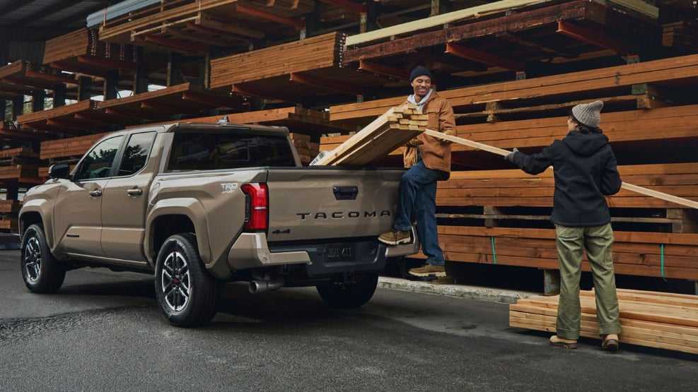 A brown Toyota Tacoma being loaded up with wooden planks.