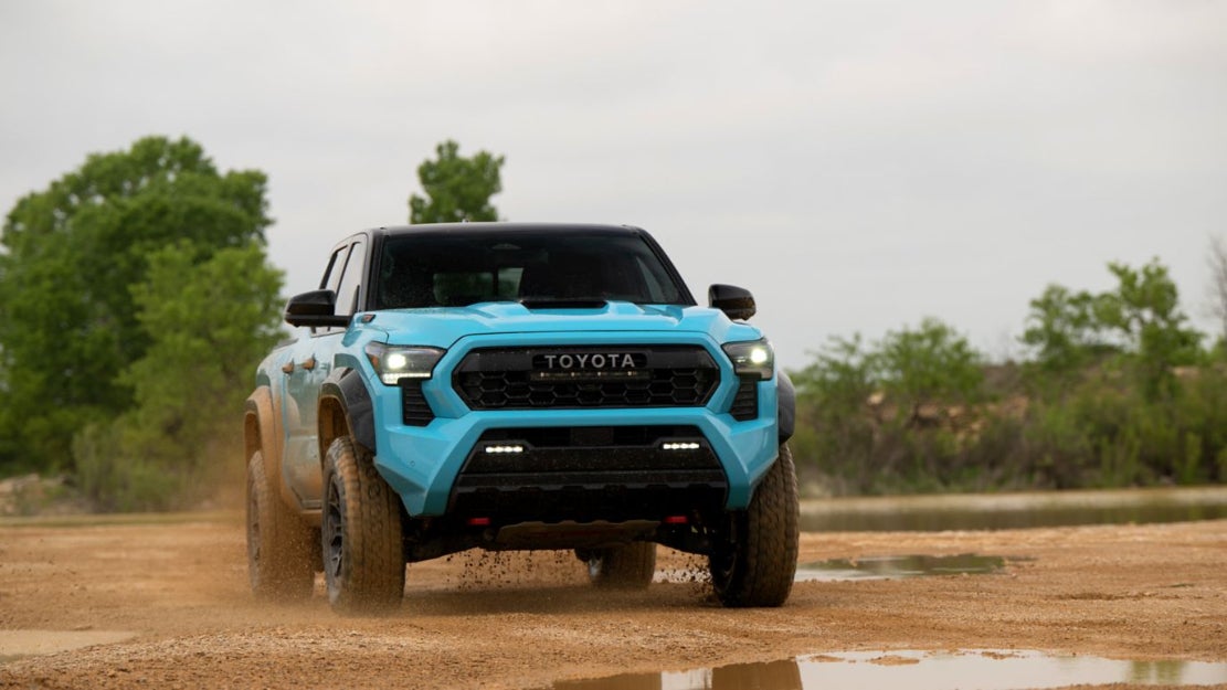 A light blue Toyota Tacoma driving over muddy ground.